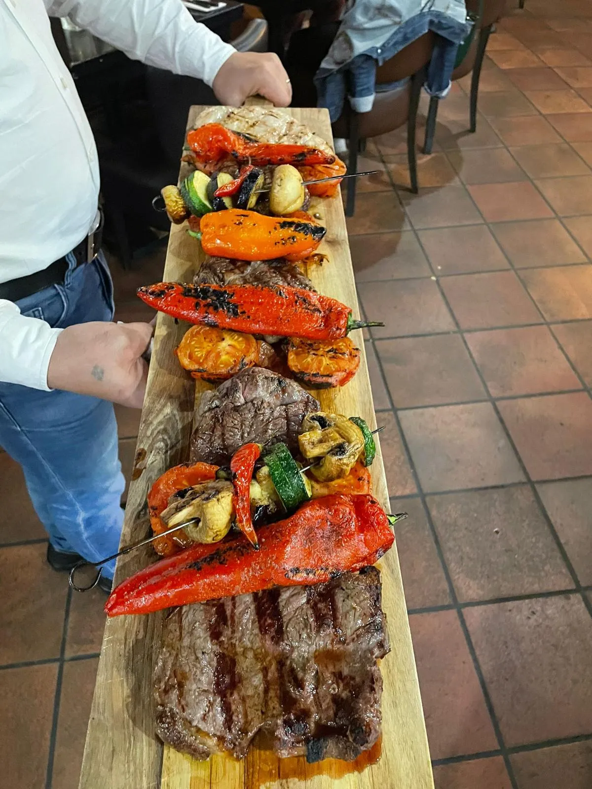 Houten plank met gegrilde steaks en gegrilde paprika wordt naar tafel gebracht
