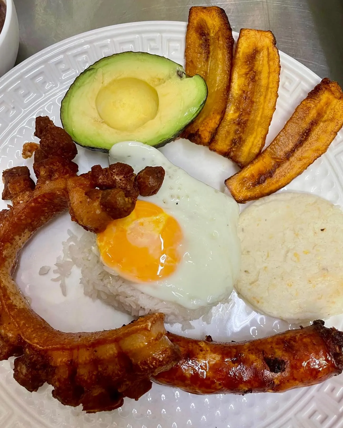 Bandeja paisa: chicharrón, chorizo, spiegelei, rijst, arepa, bakbanaan, halve avocado, bonen in het bakje links