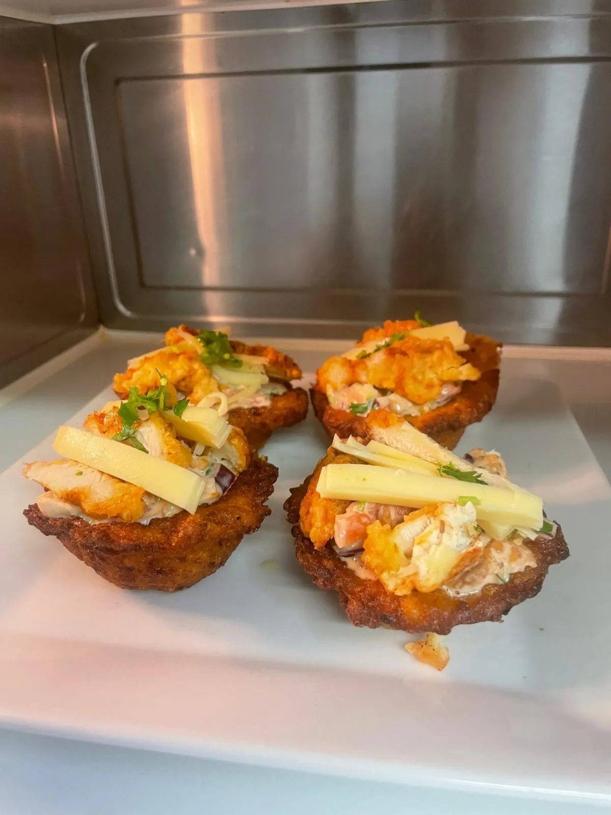 Drie gefrituurde patacón-bakjes gevuld met kip, salsa en kaasreepjes