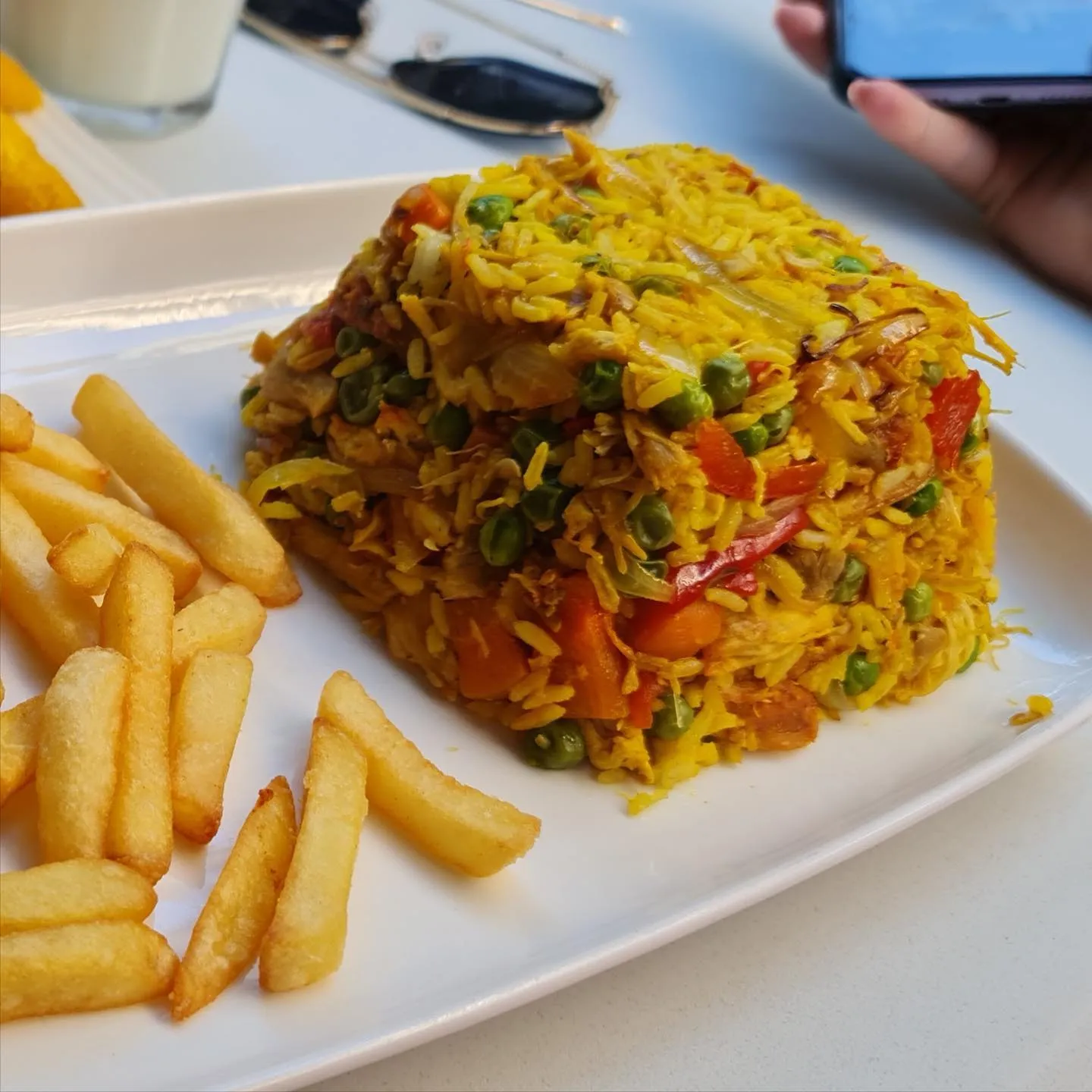Arroz con pollo, opgestapeld, met friet ernaast en een glas melkachtig drankje